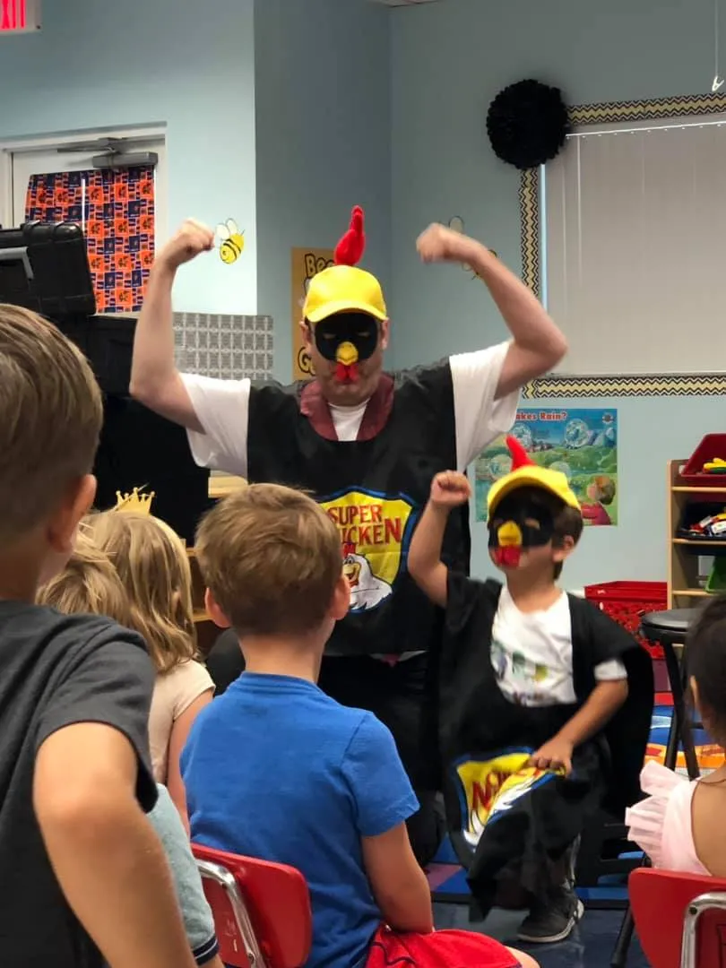 Eric The Magic Guy on stage with a young helper, both in costume, in front of seated kids